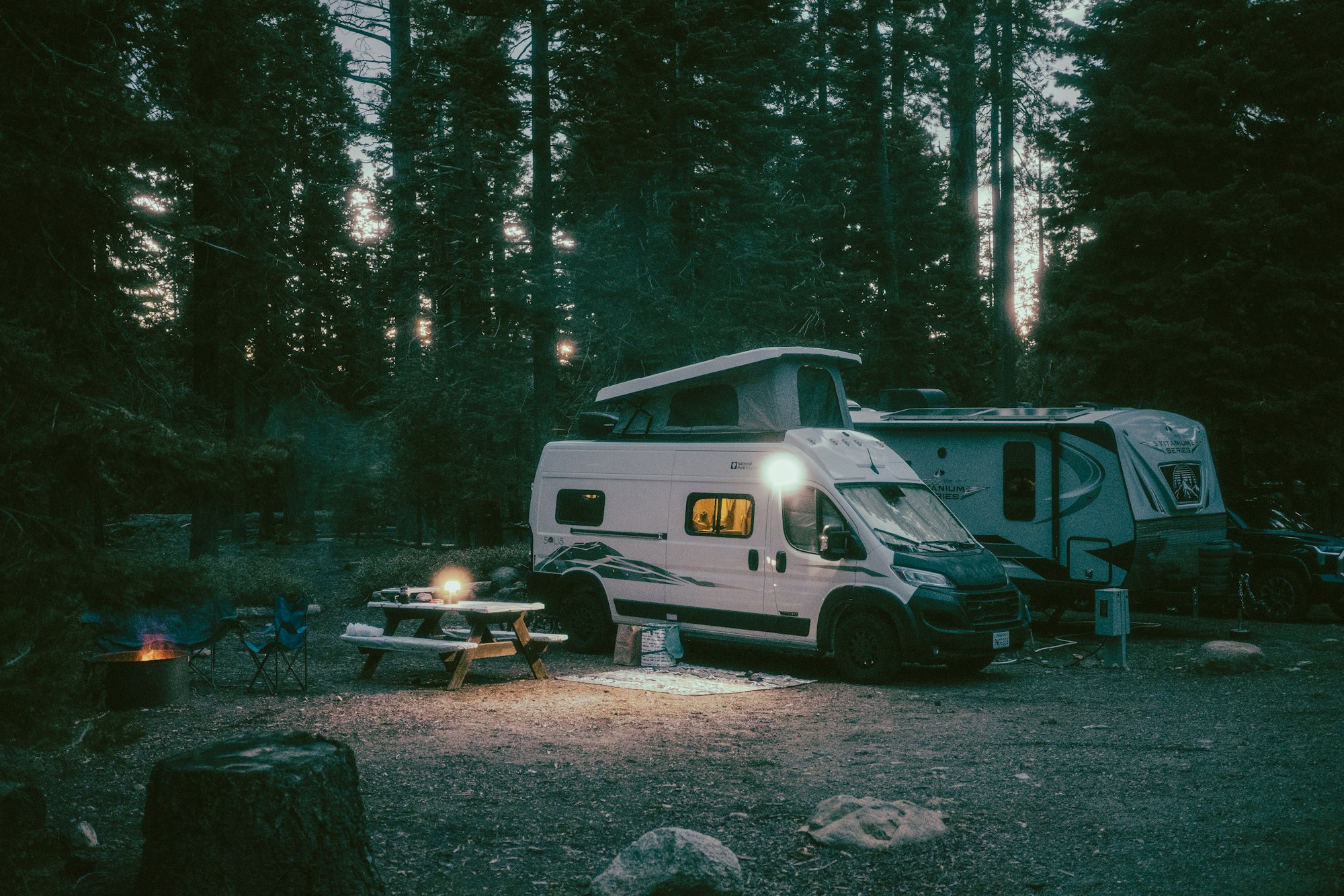 An RV set up at a wooded campsite at dusk