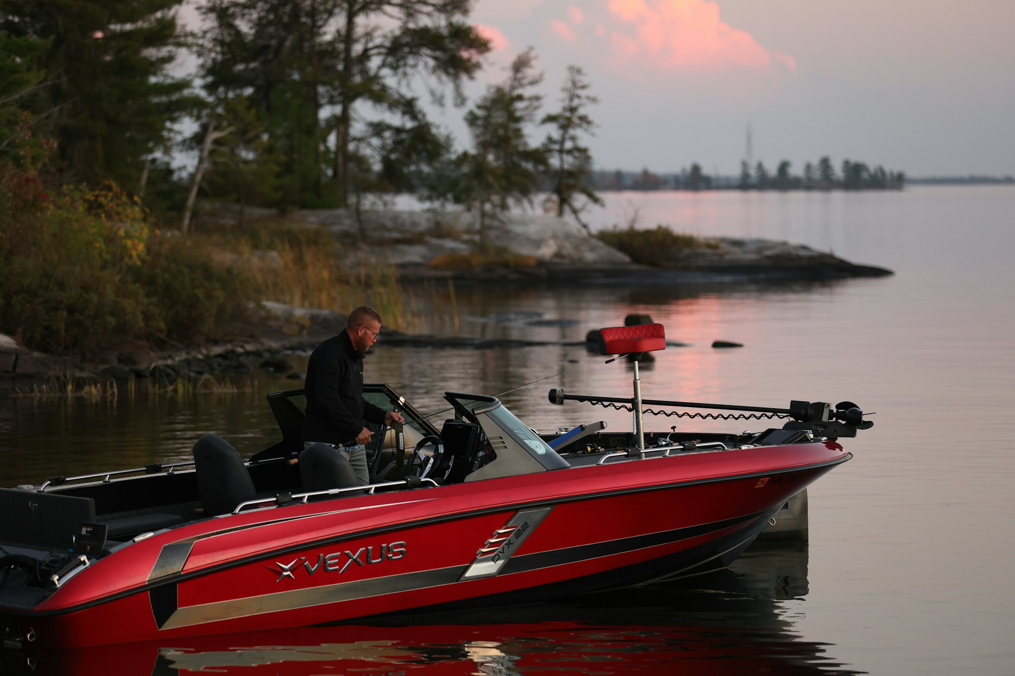 A red Vexus fishing boat with its outboard at the shoreline